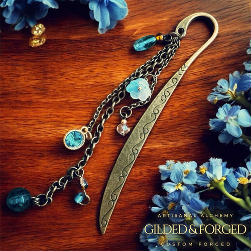 Antique brass bookmark with blue crystal beads and floral charms on wooden surface with blue flowers