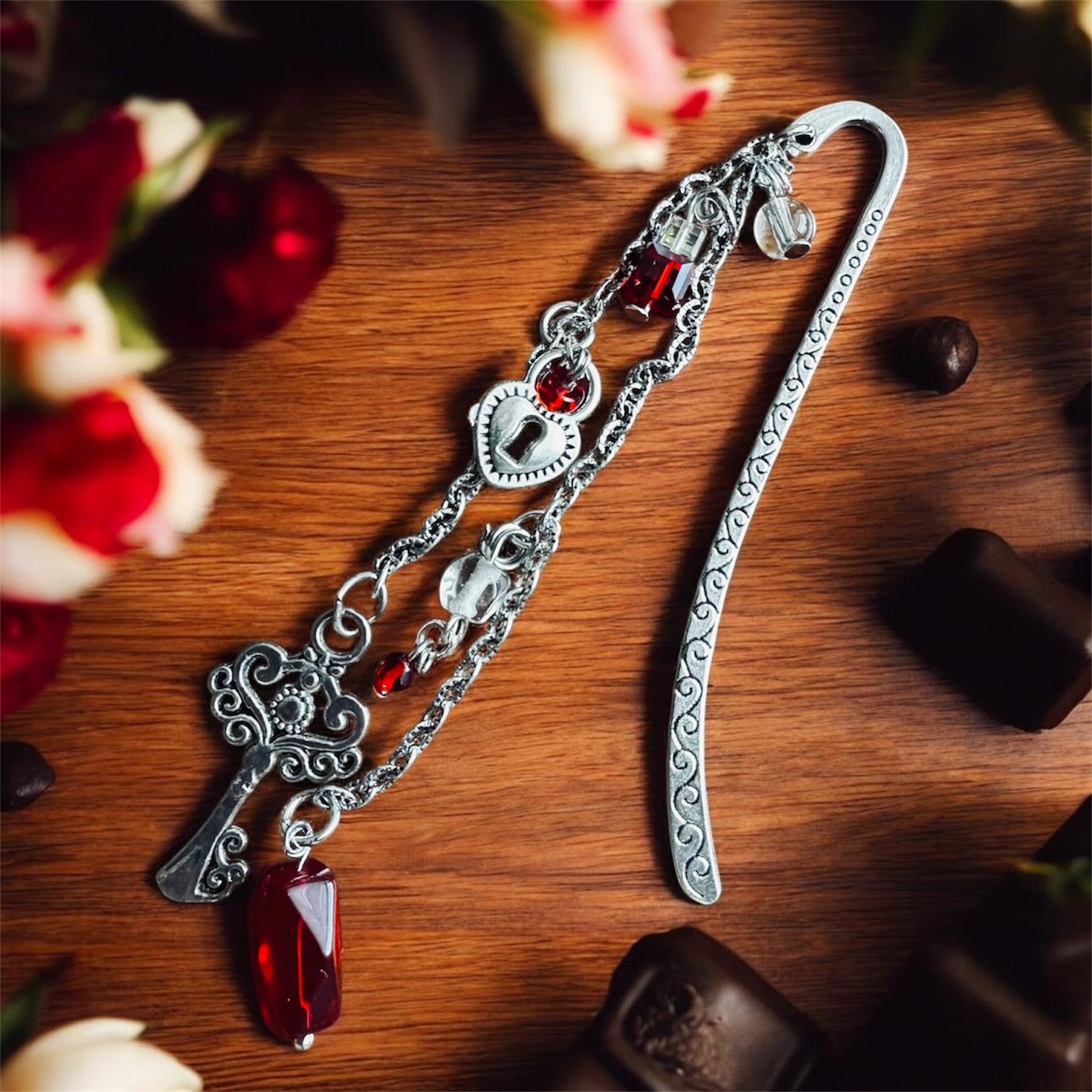 Silver heirloom bookmark with vintage red crystals, heart charm, and chain details on wooden surface with roses