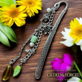 Silver heirloom bookmark with vintage glass leaf charm, green beads, and floral accents on wooden surface with flowers