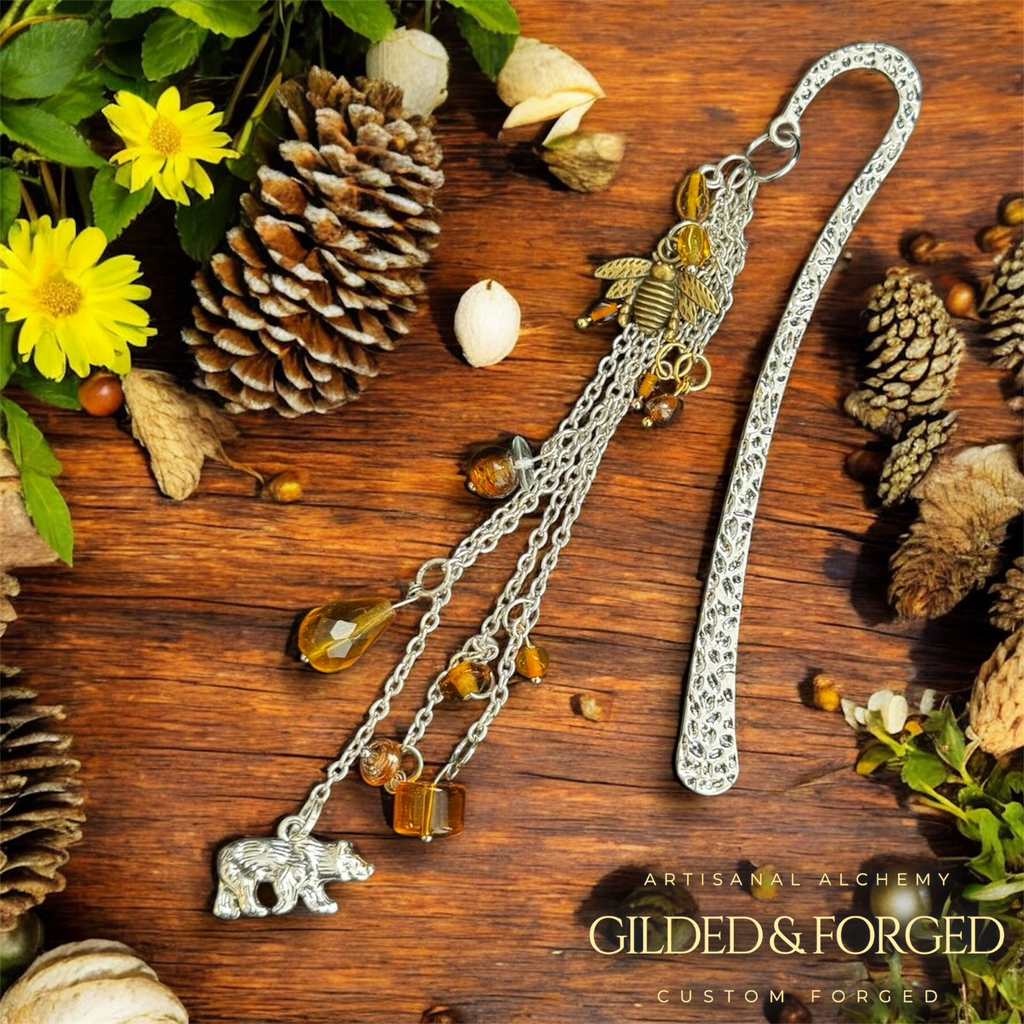 Silver heirloom bookmark with amber beads, bee and bear charms on wooden surface with pinecones and leaves